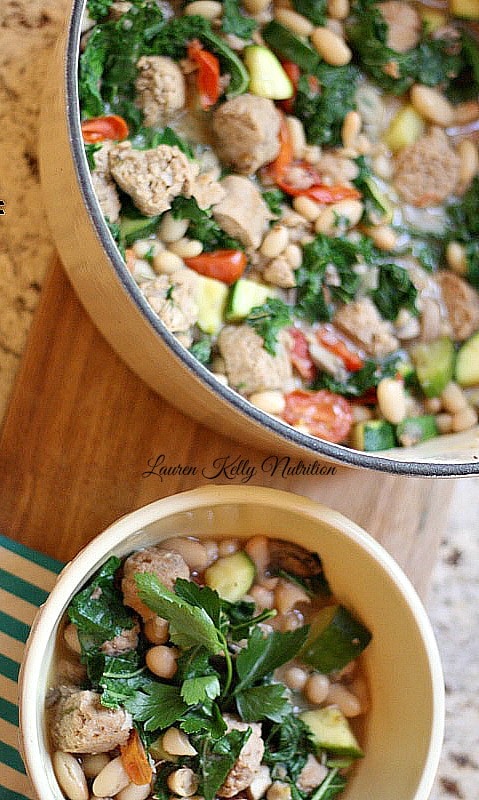 This Kale White Bean and Sausage Stew  in a large pot with a small bowl in front.