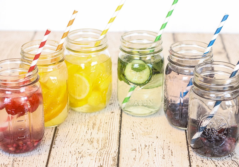 Horizontal picture of rainbow colors of waters in mason jars with matching rainbow color striped straws.