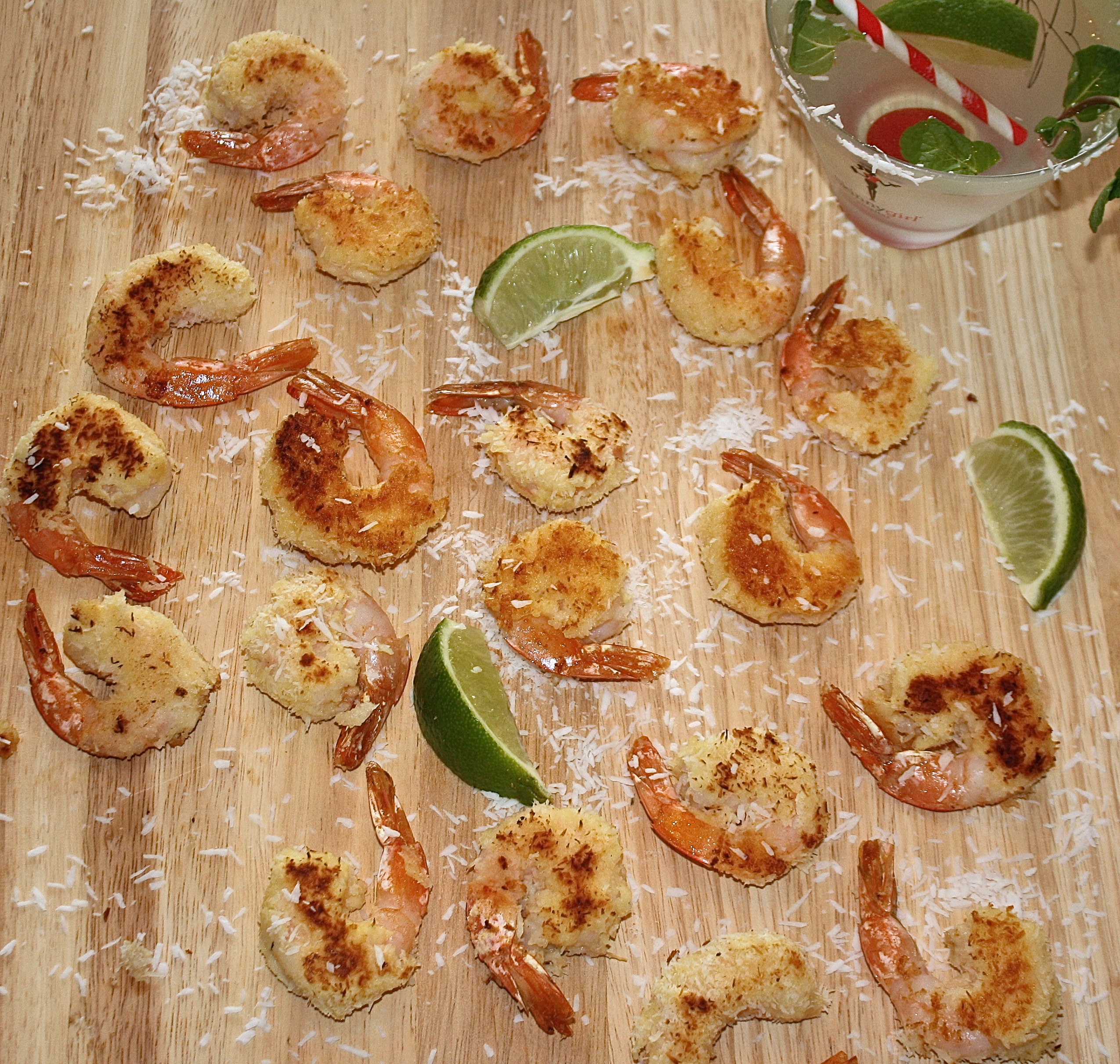 Scattered coconut lime shrimp on a wood board with sliced limes.
