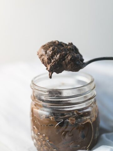 Side view picture of a big spoonful of avocado chocolate pudding on top of a clear jar filled with pudding.