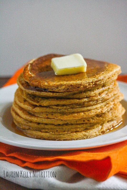 Close up of a stack of pumpkin protein pancakes on a white plate with a pat of butter on top.