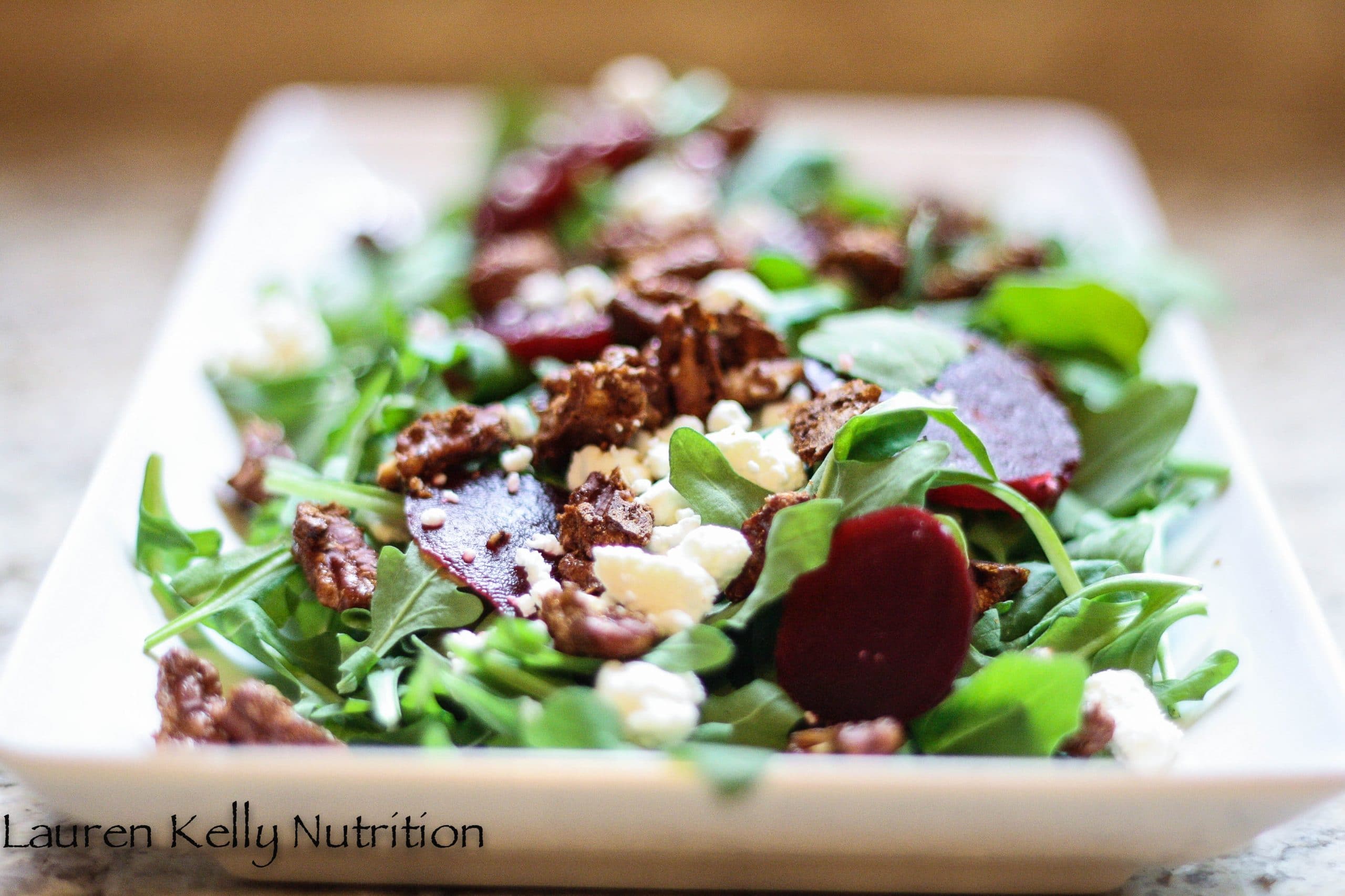 Horizontal picture of salad in a rectangular white platter which is vertical and all of the arugula beet salad in the platter.