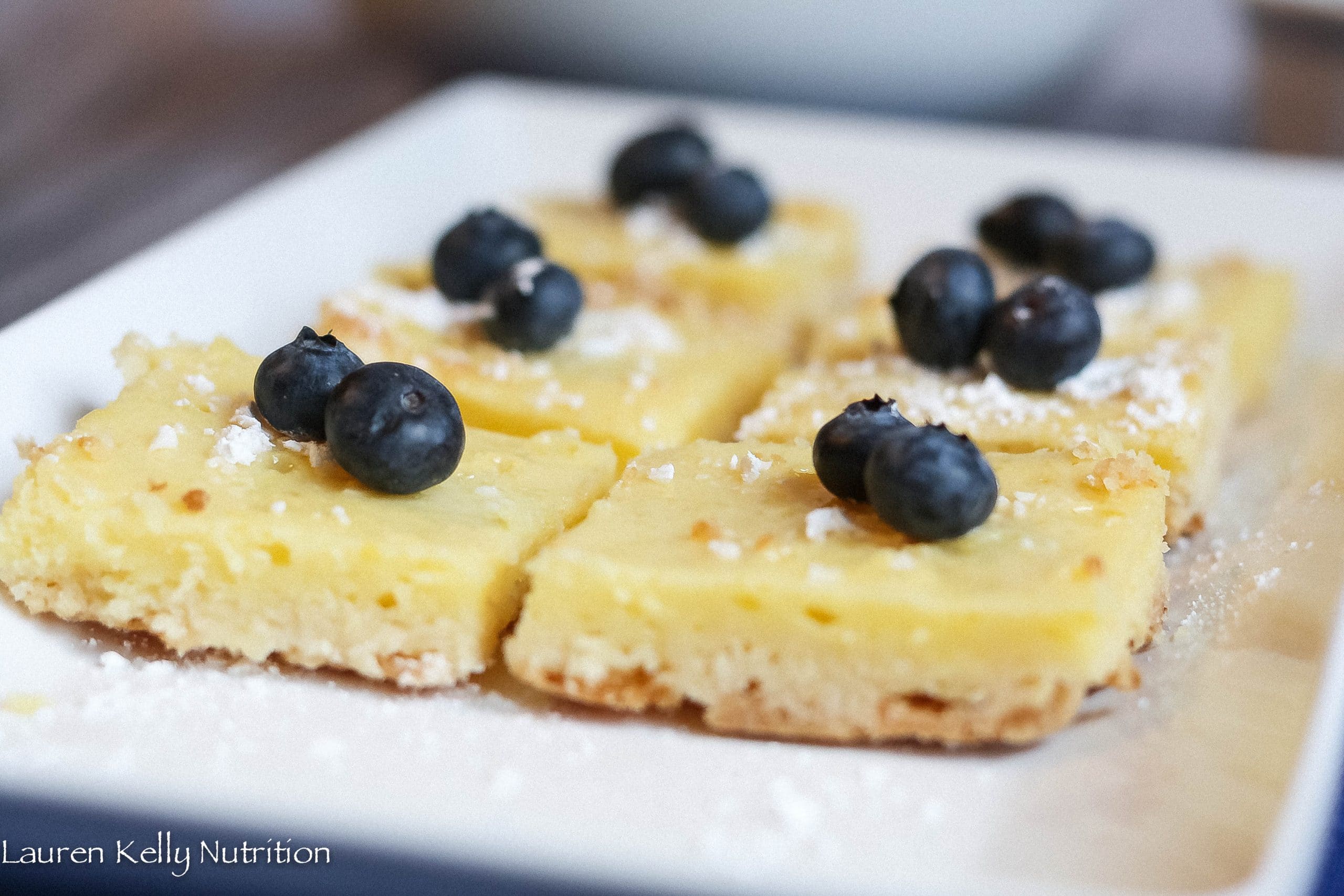 Horizontal picture of lemon bars with blueberries on top on a white plate.