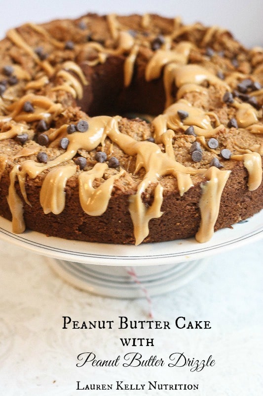Close up of peanut butter cake on a white cake stand with peanut butter drizzle and chocolate chips on top.