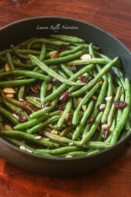 Picture of balsamic glazed green beans with cranberries and almonds in a dark grill pan on a wooden background.