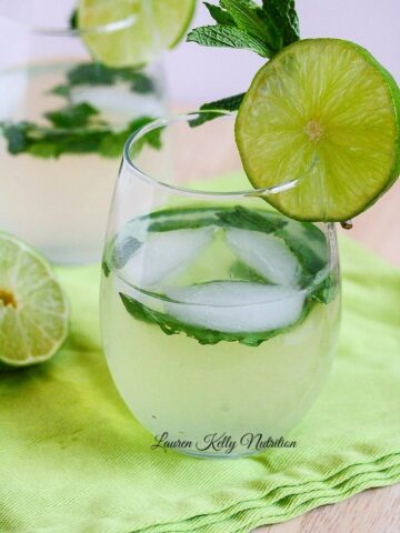 Close up on mojito wine spritzer with mint leaves floating in the glass and lime piece on the rim of glass.