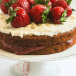 Vanilla layer cake on a pedestal stand with strawberries on top.