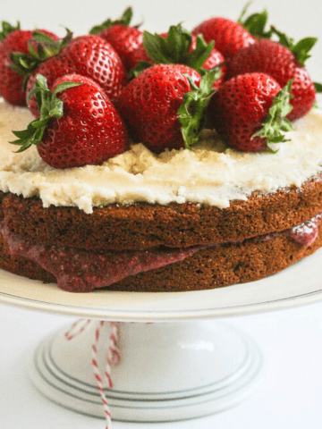 Vanilla layer cake on a pedestal stand with strawberries on top.