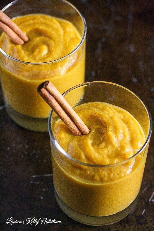 Close up picture of the tops of two glass jars with pumpkin mousse inside, one cinnamon stick coming out the side of each jar on a dark background.