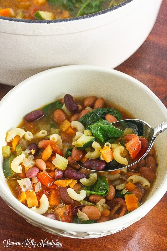  Picture of minestrone soup in a white bowl with a spoonful of soup on the spoon.