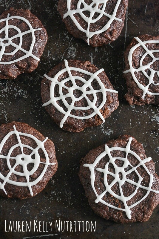 Overhead picture of chocolate cookies with spiderweb white icing on top.