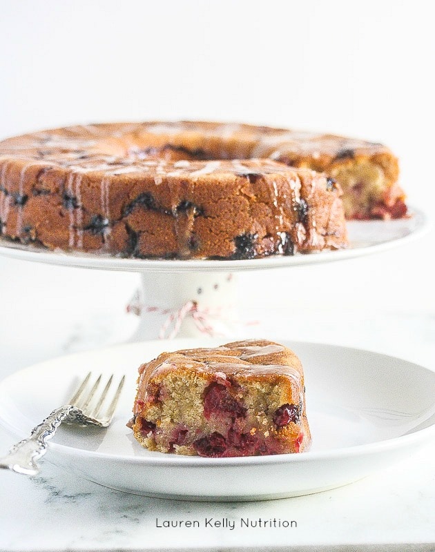 Cranberry Cake on a white stand with a slice in front on a white plate.