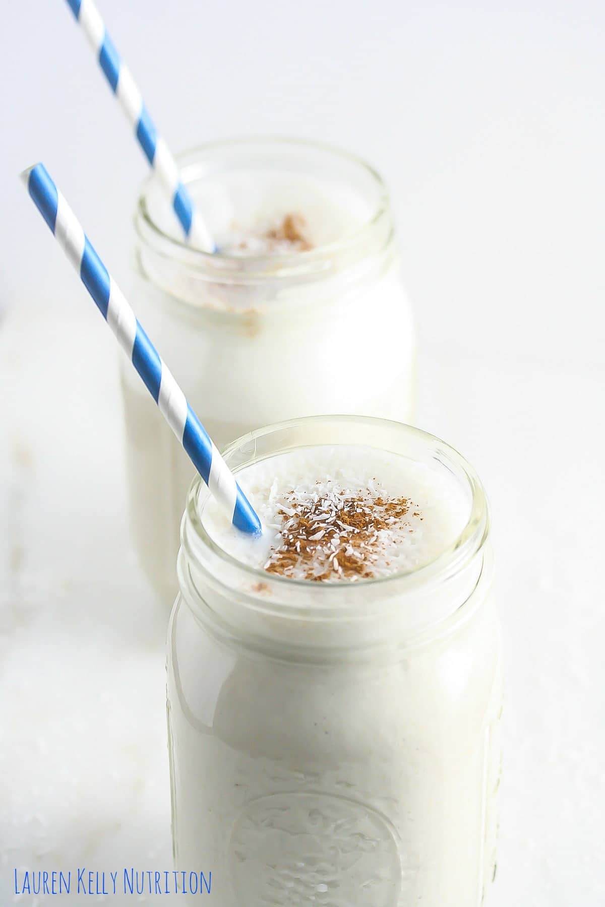 Coconut quinoa smoothie in two mason jars with blue and white striped straws.