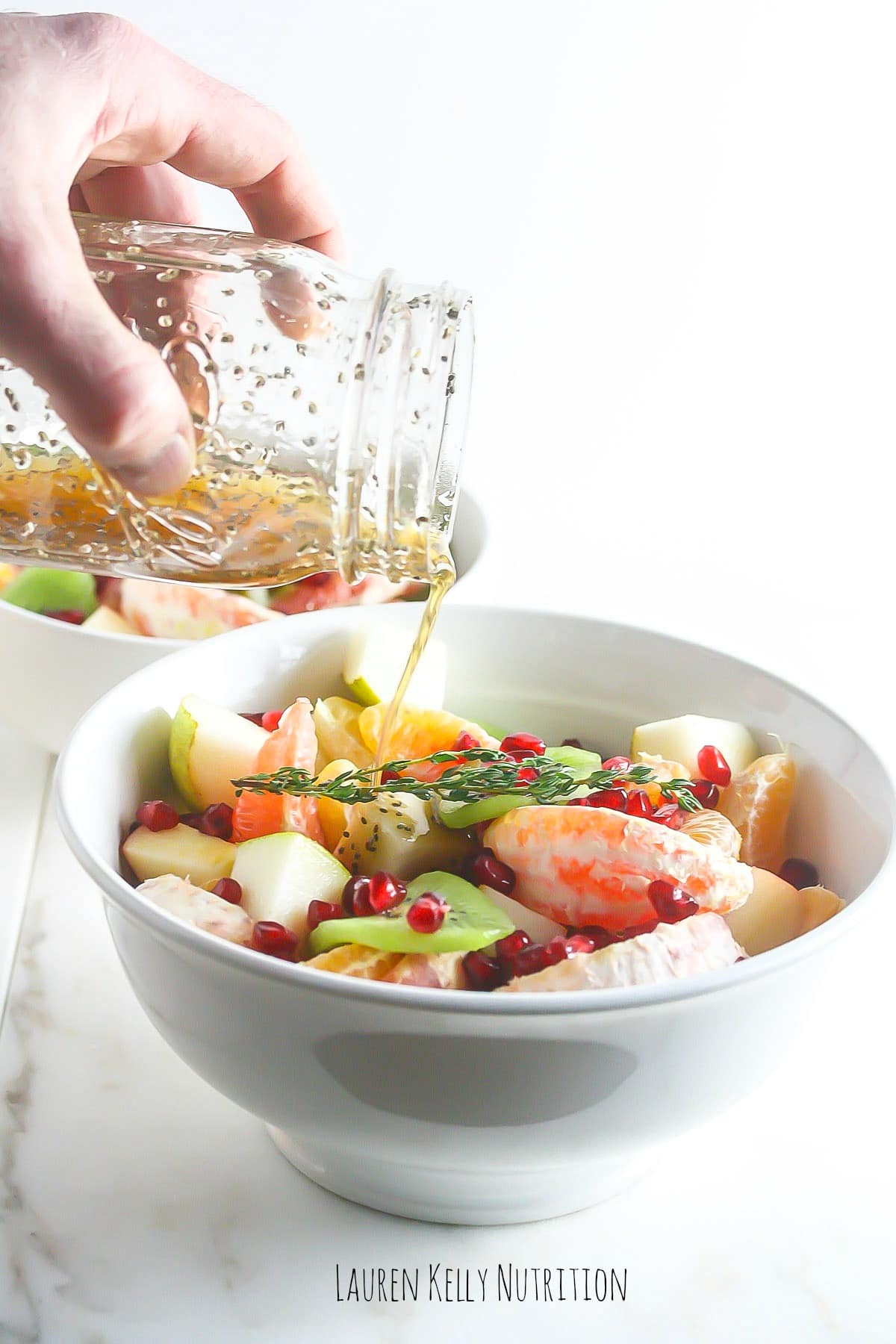 Pouring the Ginger Chia Dressing from a clear jar onto winter fruit salad.