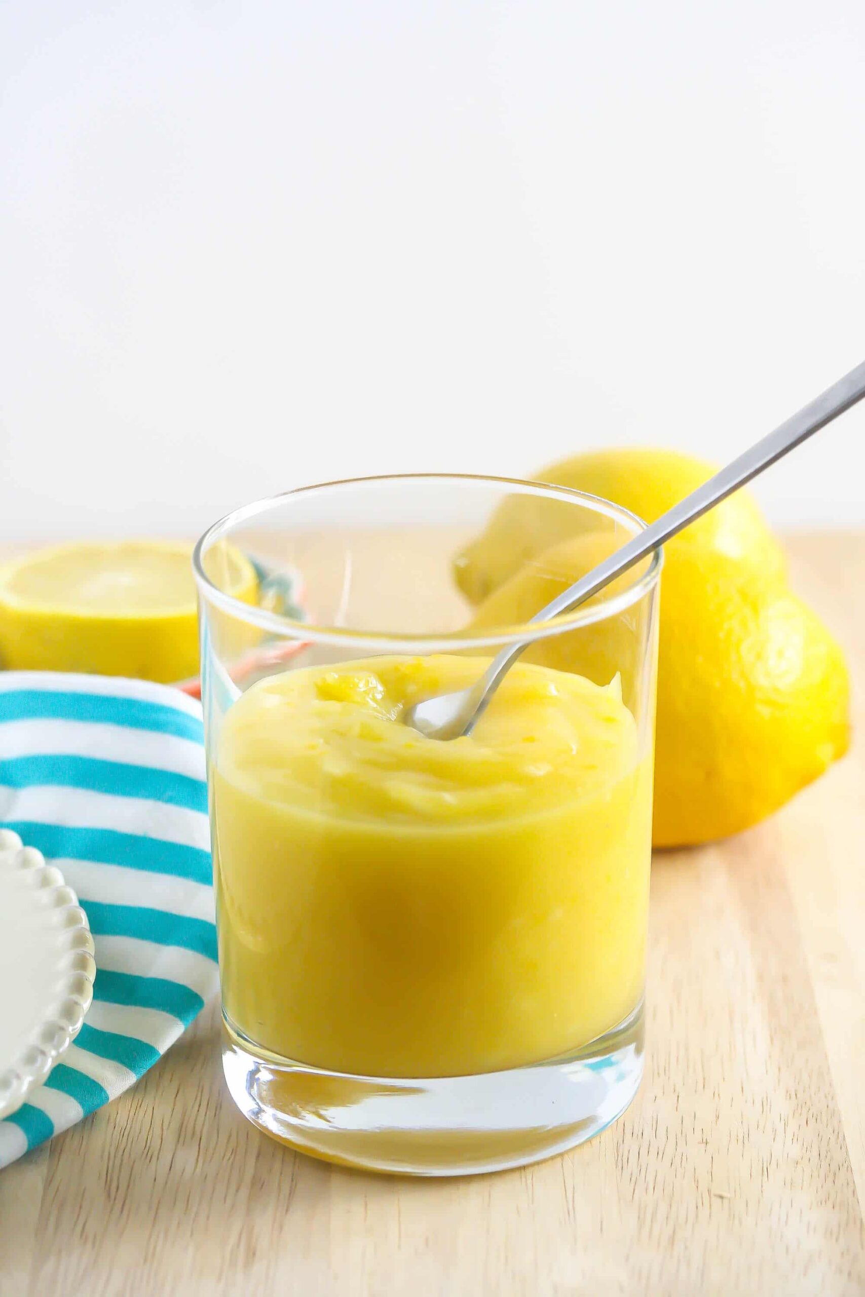 Lemon Curd in a glass with a spoon coming out of it.