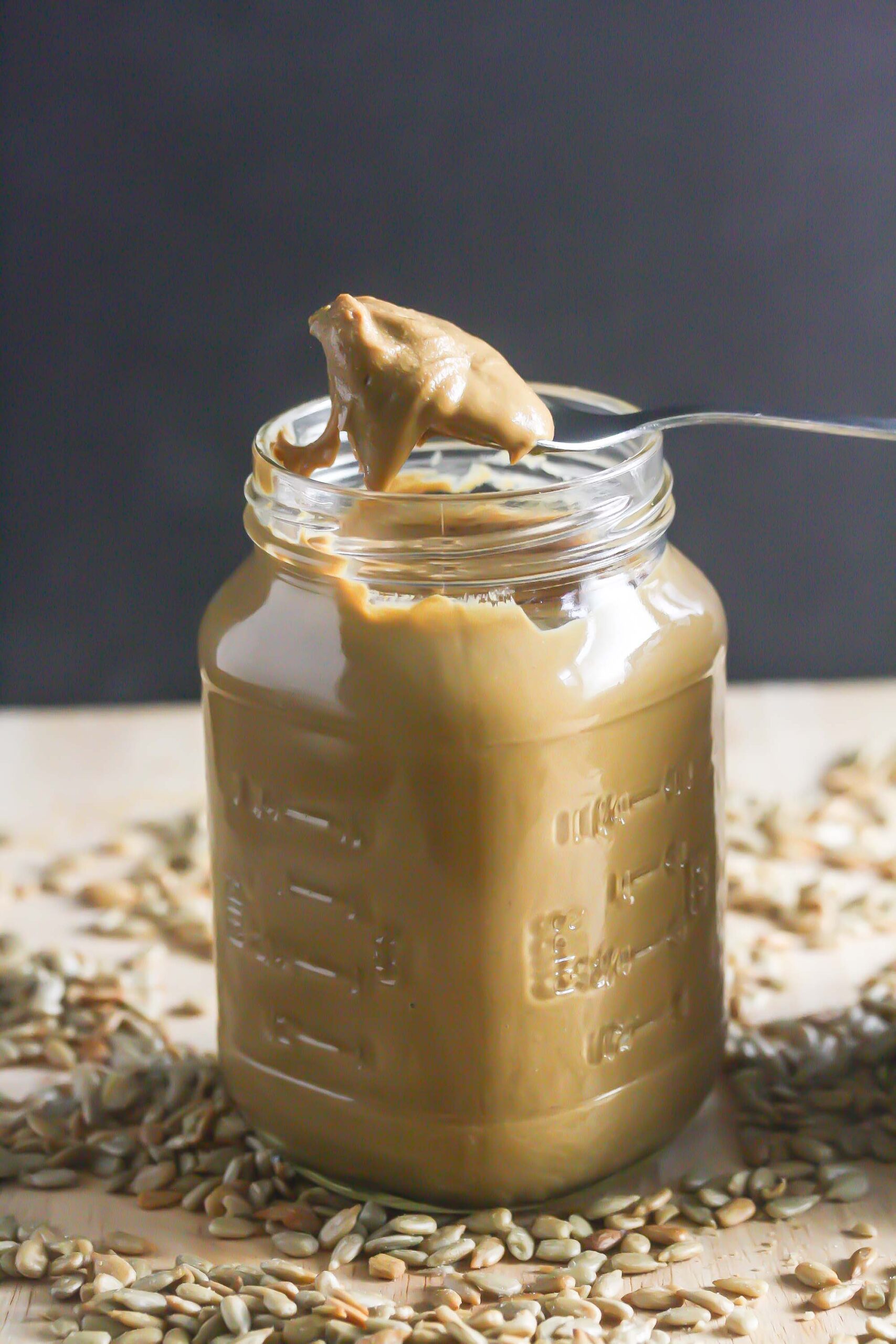 Sunflower Seed Butter in a glass jar with a spoon coming out of it and sunflower seeds scattered around.