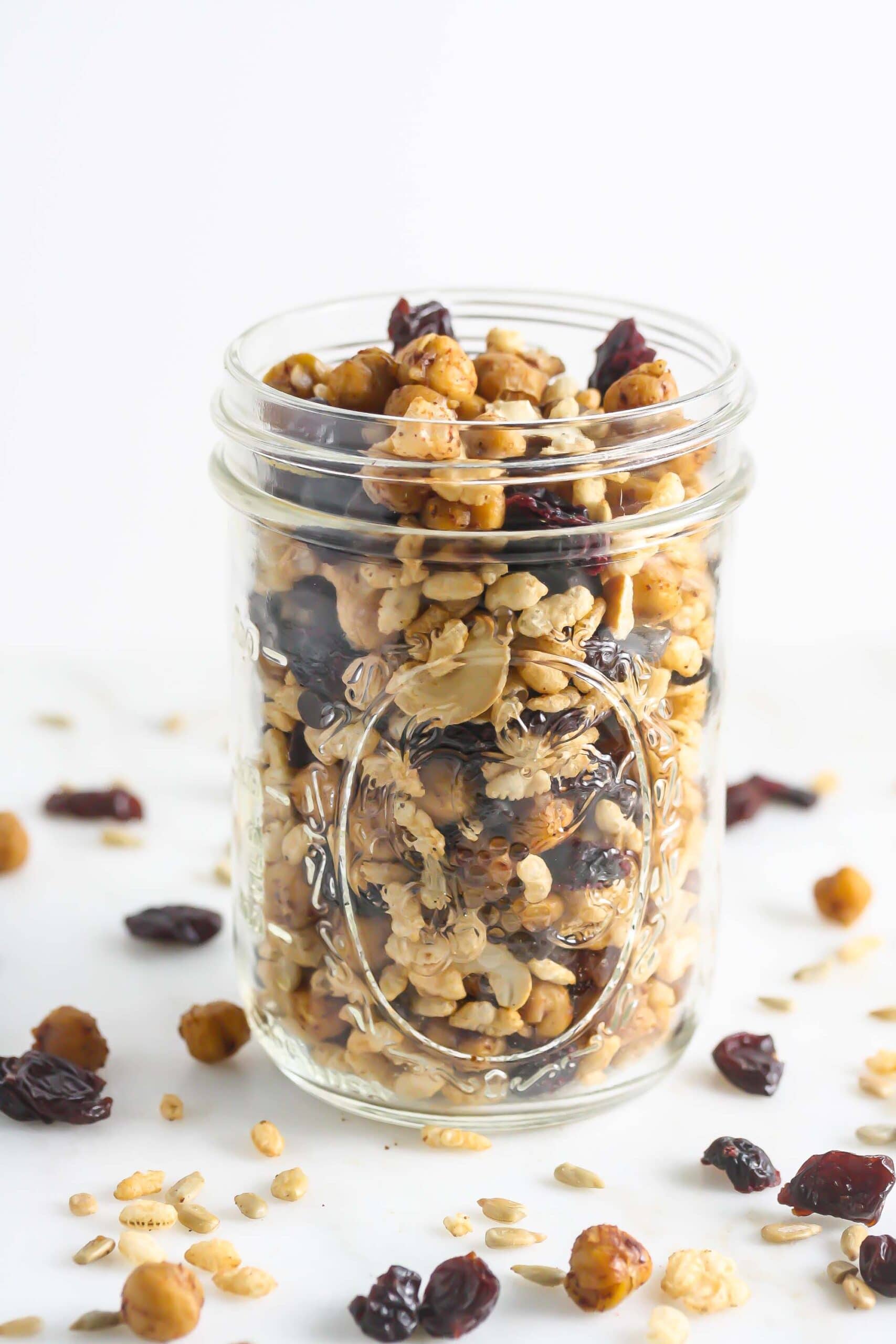 Roasted chickpea trail mix in a clear jar and some scattered around it.