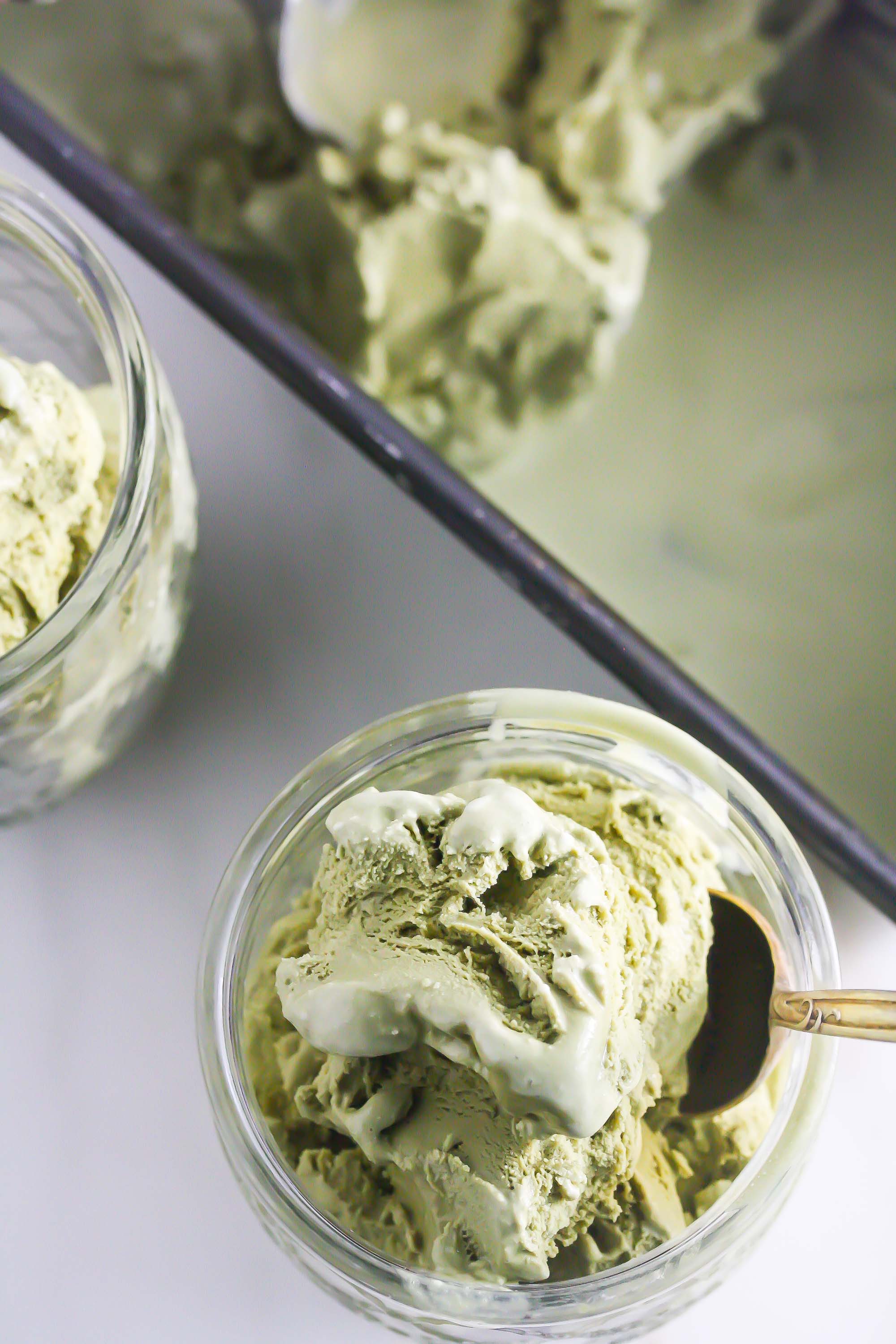 Ice cream in a jar with a spoon in it in front, more ice cream in rectangular pan in the back and another jar of ice cream to the left.