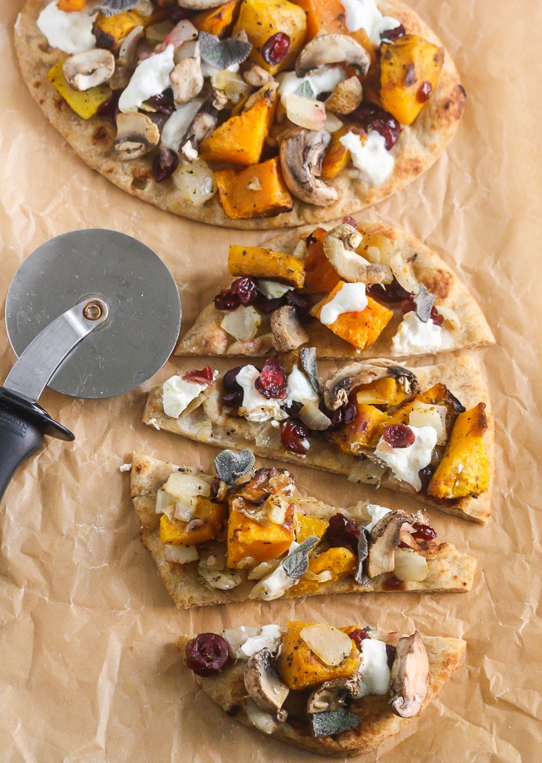 Overhead picture of butternut squash pizza cut into three slices next to a pizza cutter on parchment paper.