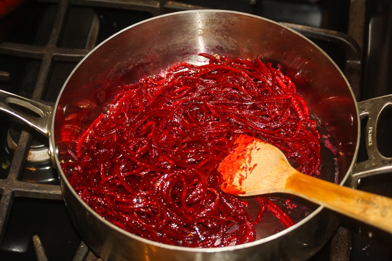 Spiralized beets in a skillet wit a wood spoon in it.