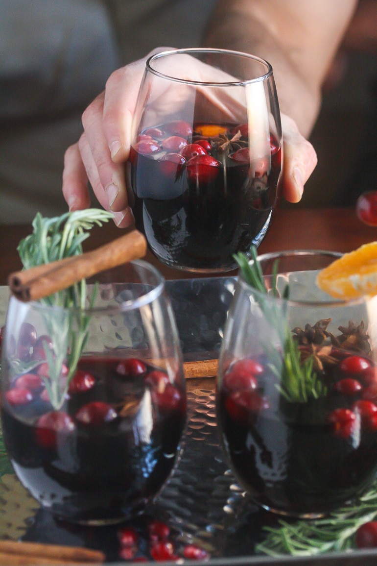 Mulled wine in clear wine gasses on a silver tray with cranberries floating and a hand holding one wine glass.