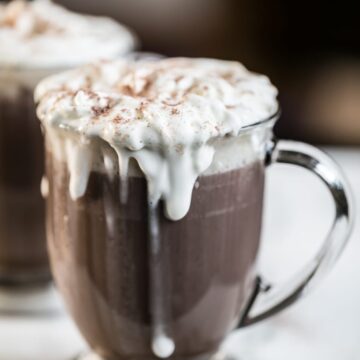 Close up of bulletproof hot chocolate in a clear glass with whipping cream dripping down the front.