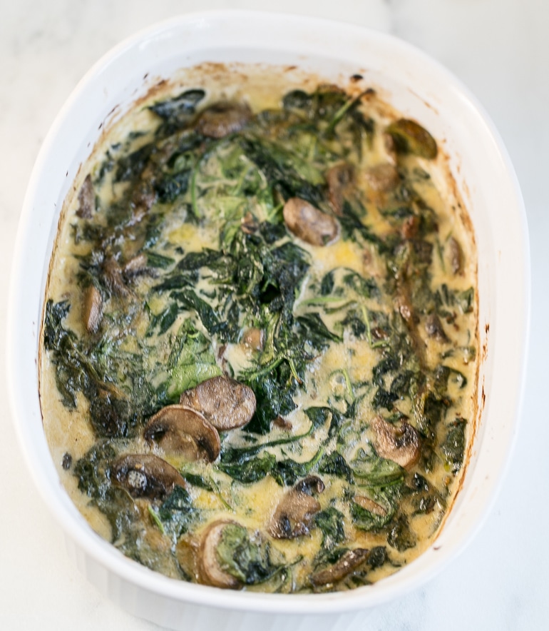 Picture of cooked spinach and mushroom gratin in white oval baking dish.