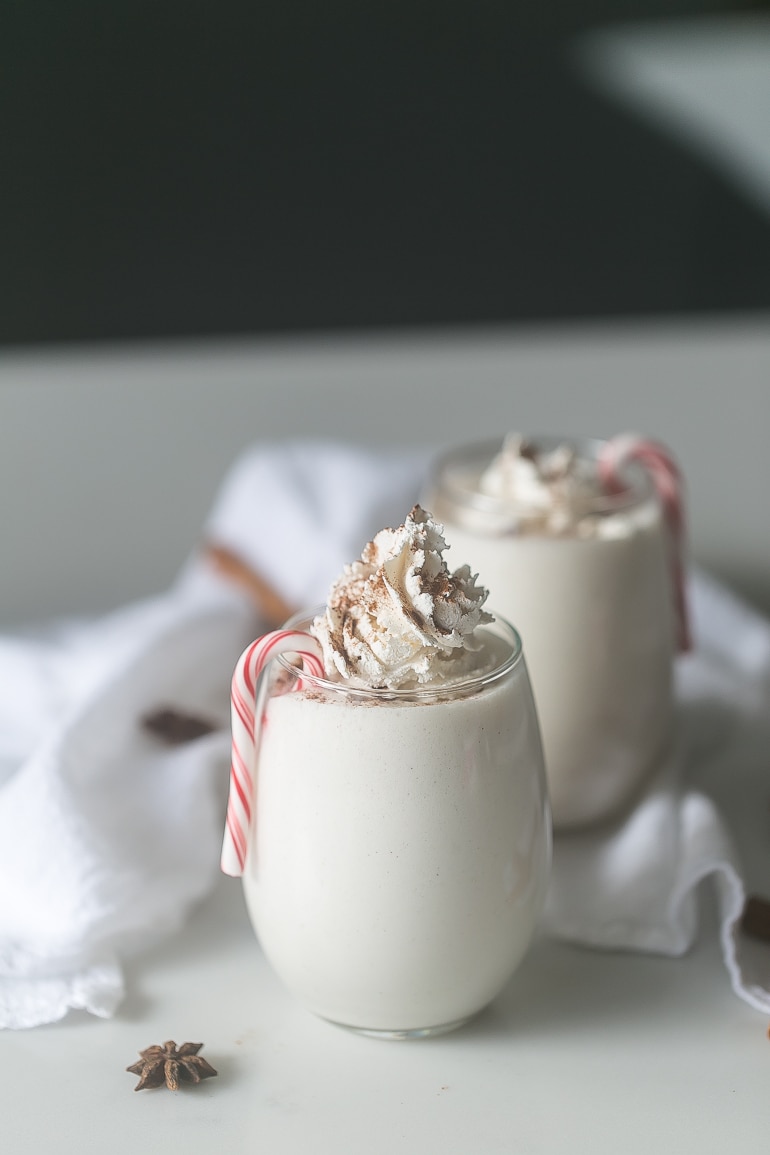 Two glasses of skinny peppermint eggnog with a small candy cane on the side and whipped cream on top.
