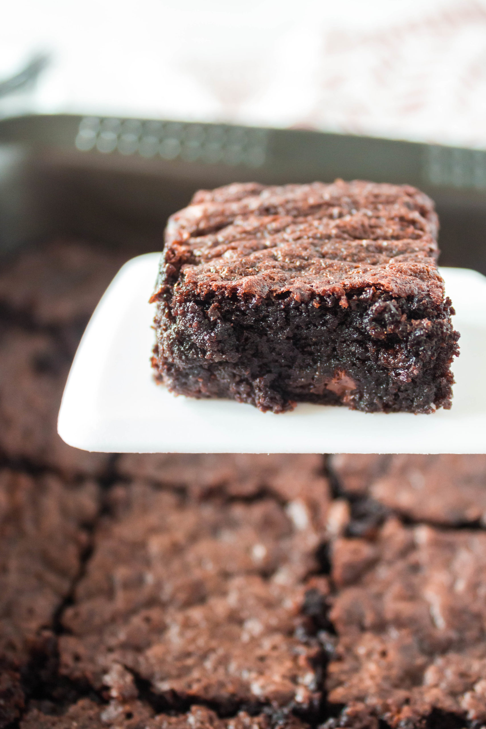 Pan of Fudgy chocolate brownies in a square baking dish with one brownie on spatula above the pan.