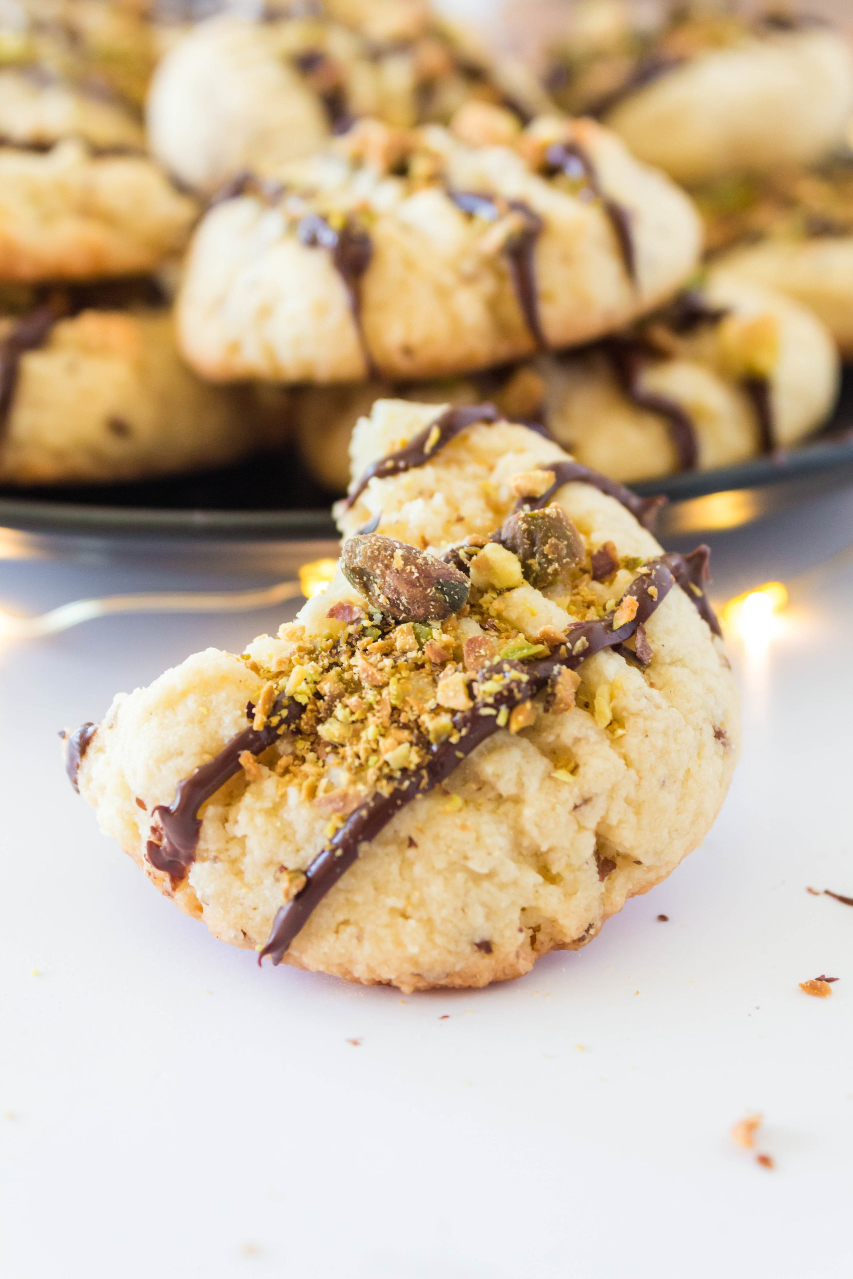 Picture of keto butter cookie with chocolate drizzle and chopped pistachios on top with a bite taken out of it.