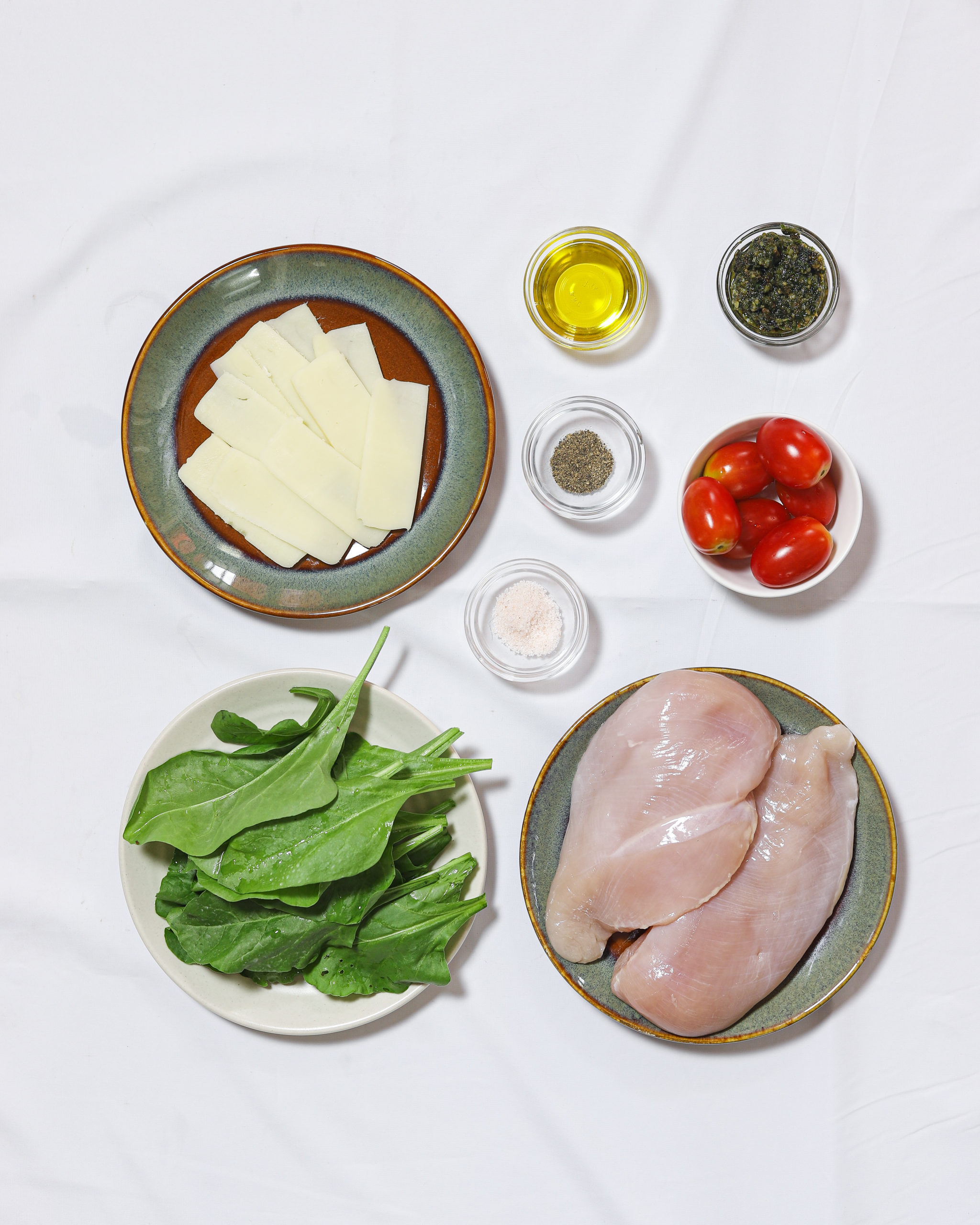 Ingredients on individual plates for stuffed chicken breasts on a white background.