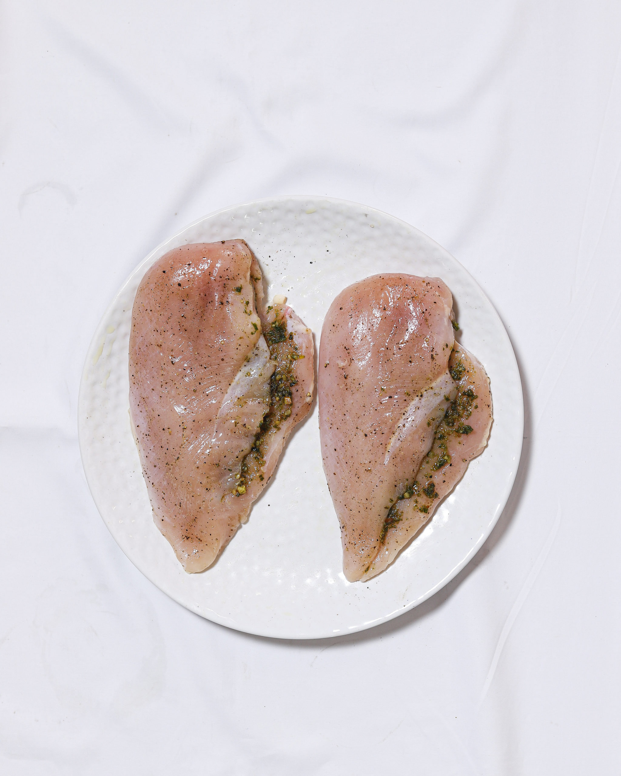 Raw chicken sliced with pesto inside on a white plate.