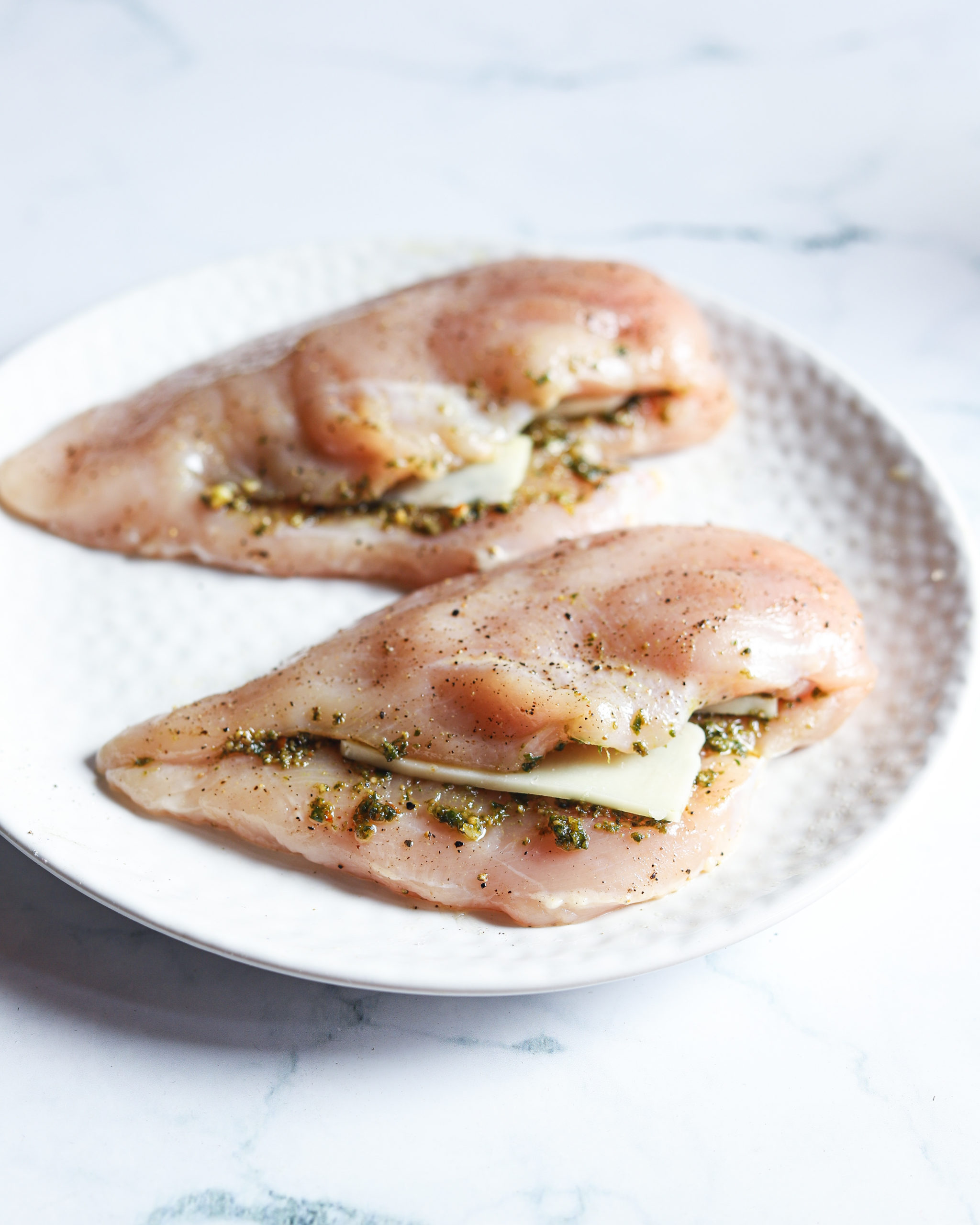 Raw chicken sliced with pesto and cheese inside on a white plate.