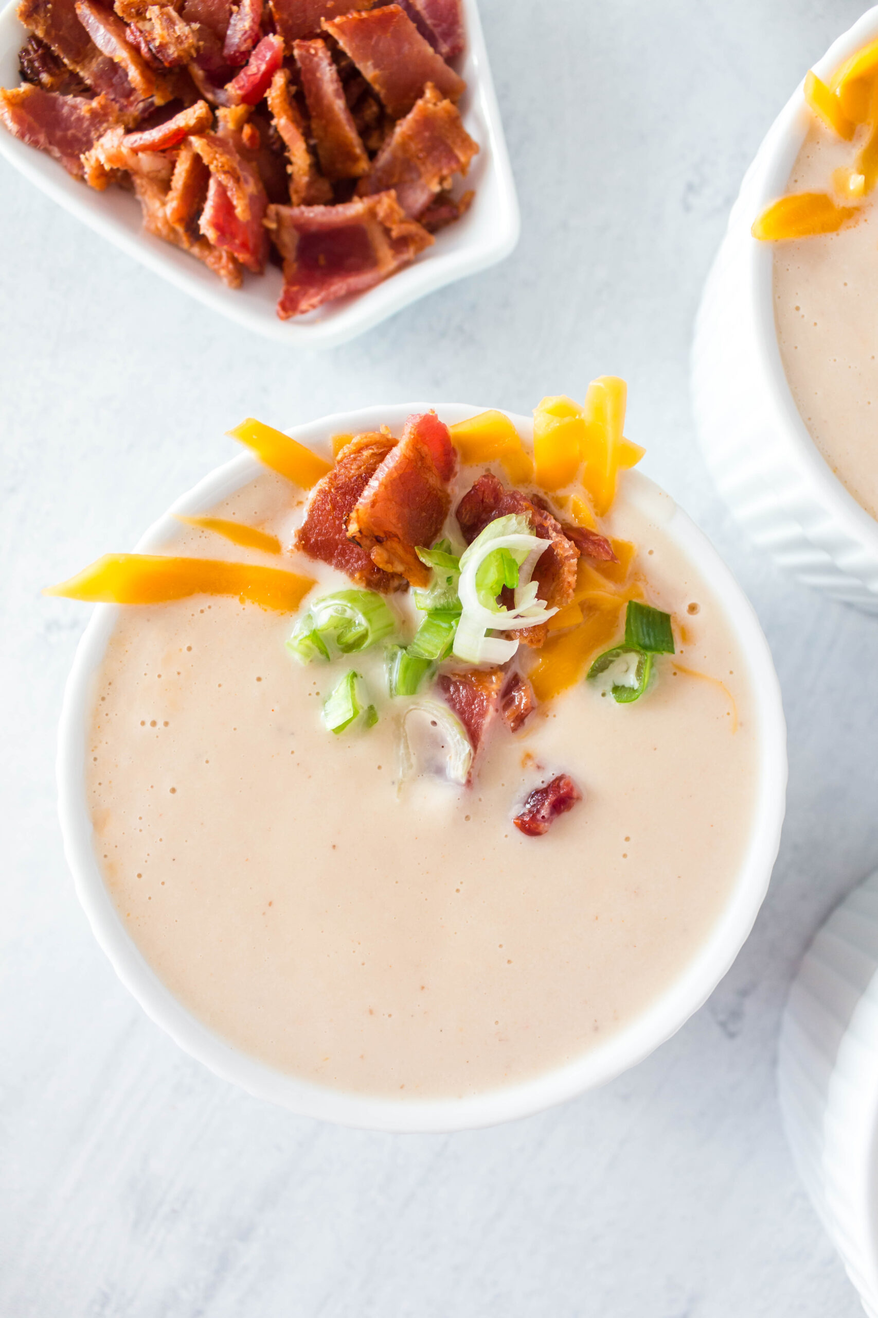 Creamy cauliflower soup in a white bowl with chopped bacon, green onions and cheese on top.
