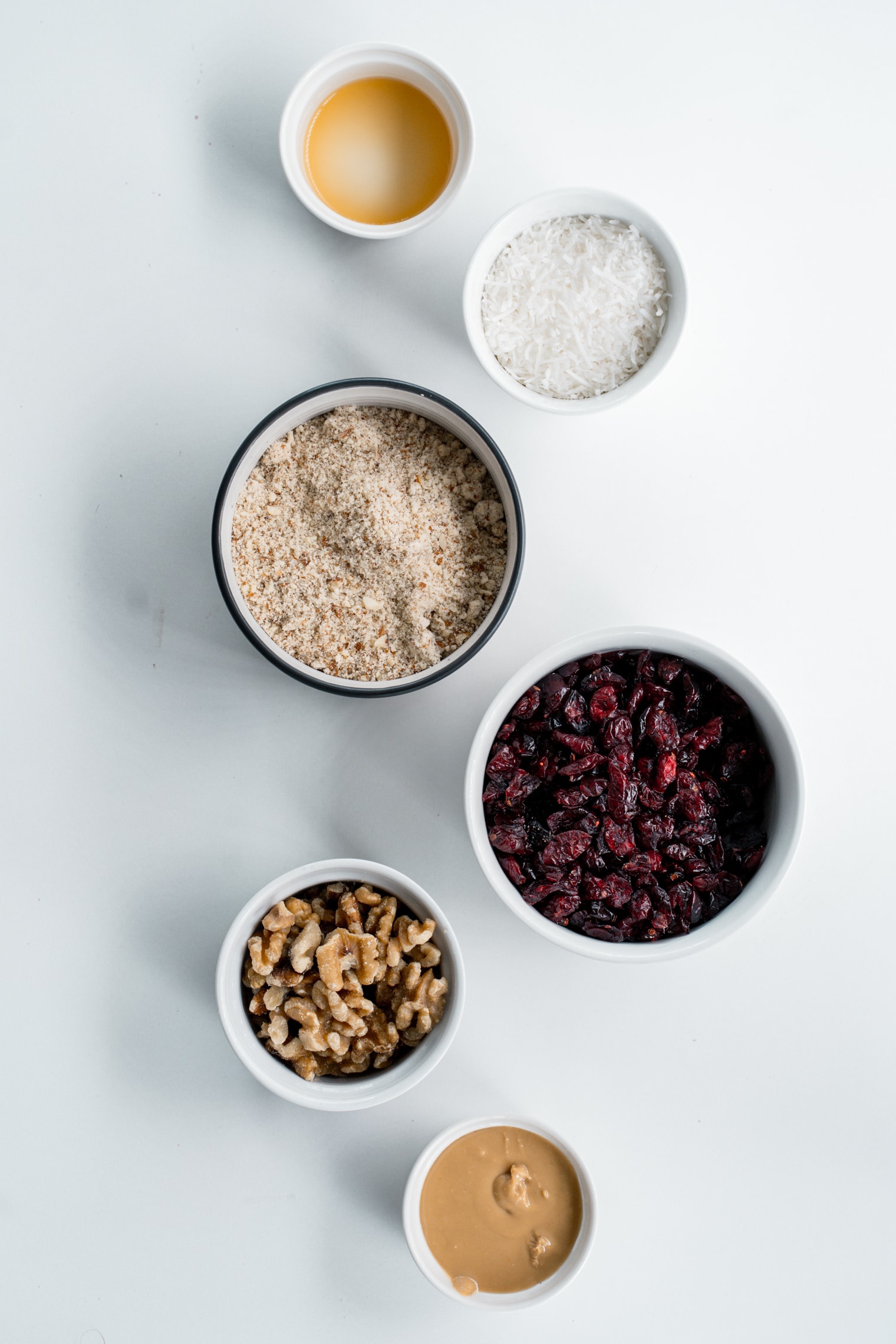 Ingredients for cranberry almond balls on a white background in individual bowls,