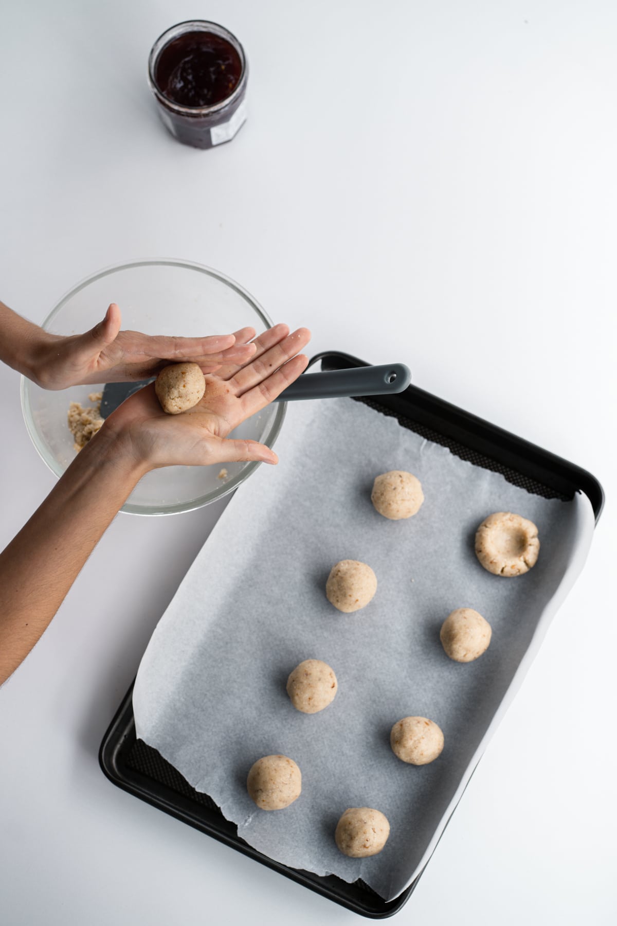 Almond flour thumbprint cookie dough on a baking sheet lined with parchment and hands above it rolling dough into balls.