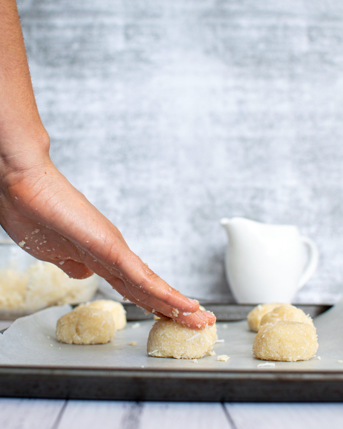 Picture of dough rolled in balls on a baking sheet lined with parchment paper and a hand pressing down on a ball.