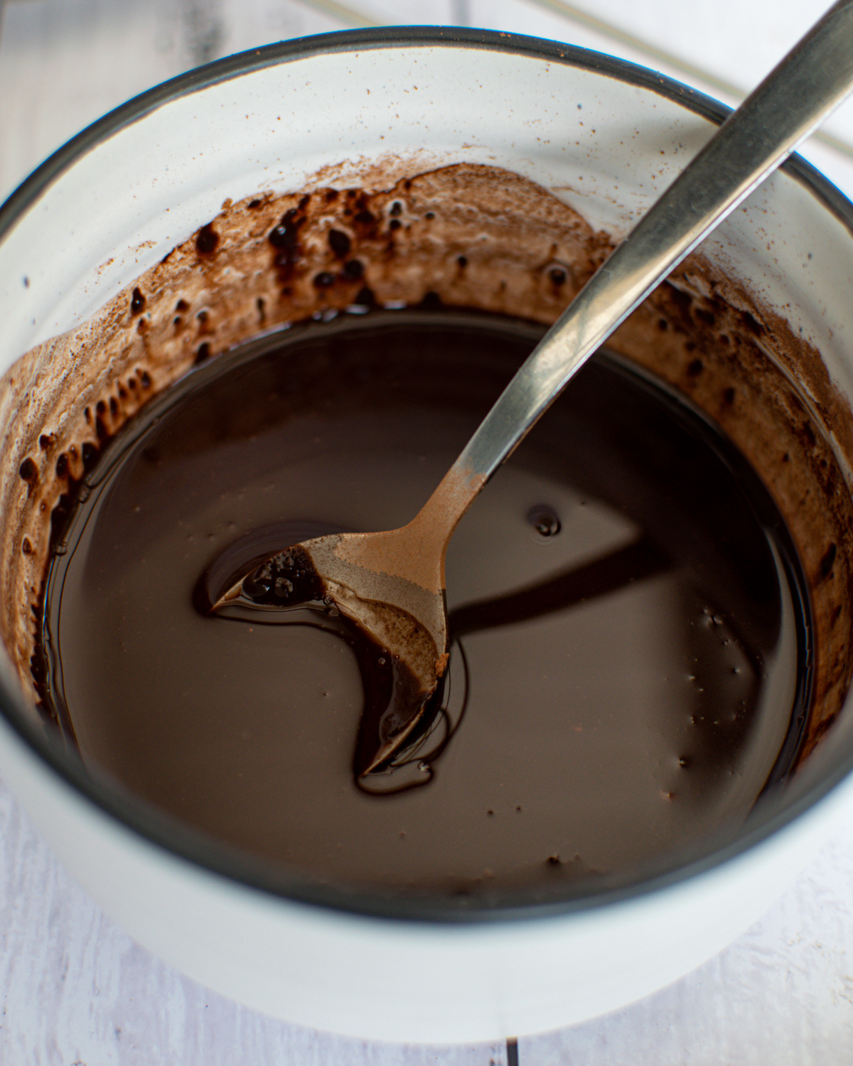 Close up of melted chocolate in a glass bowl with a big silver spoon in it.