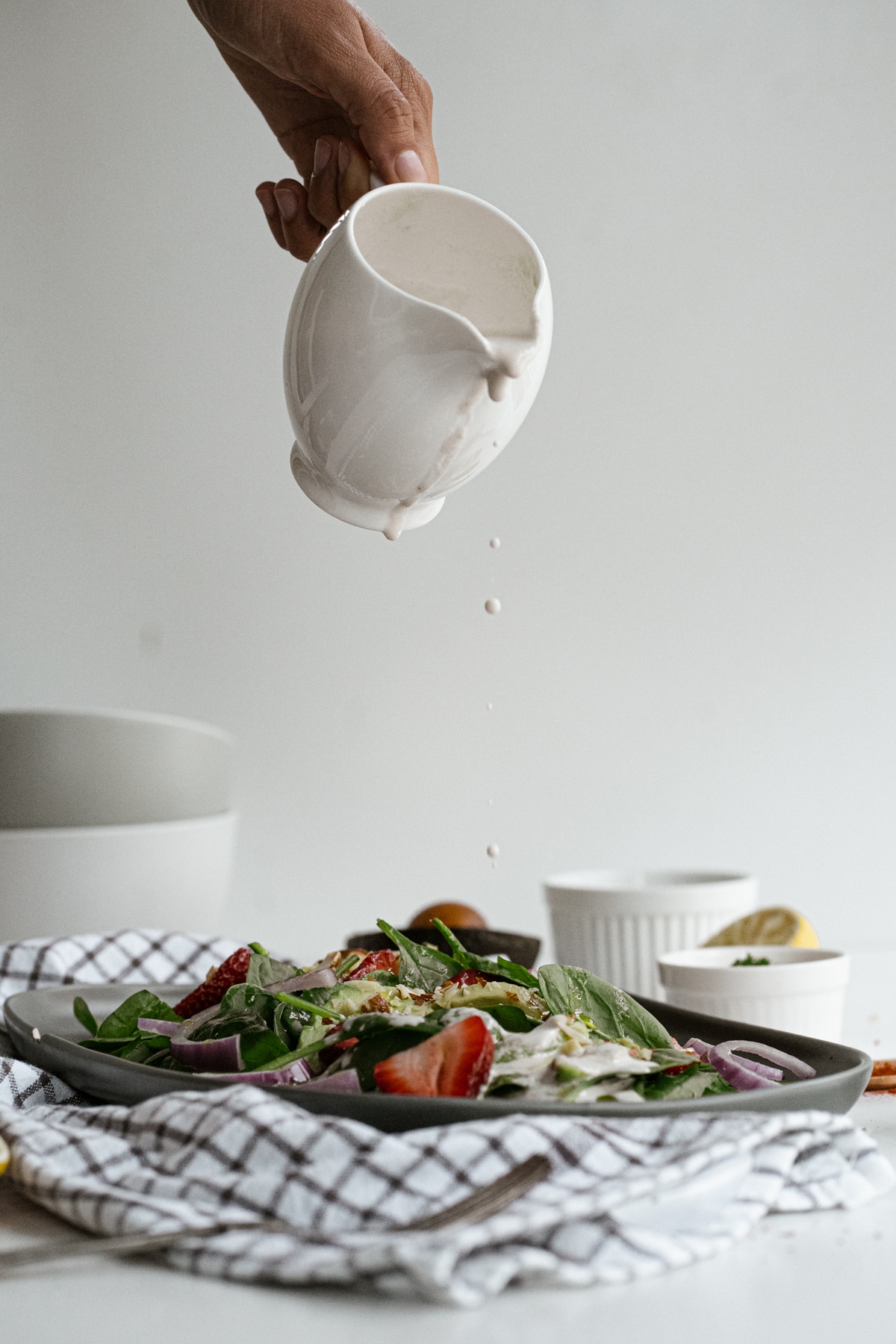 Dressing being poured from a small white pitcher onto strawberry spinach salad.