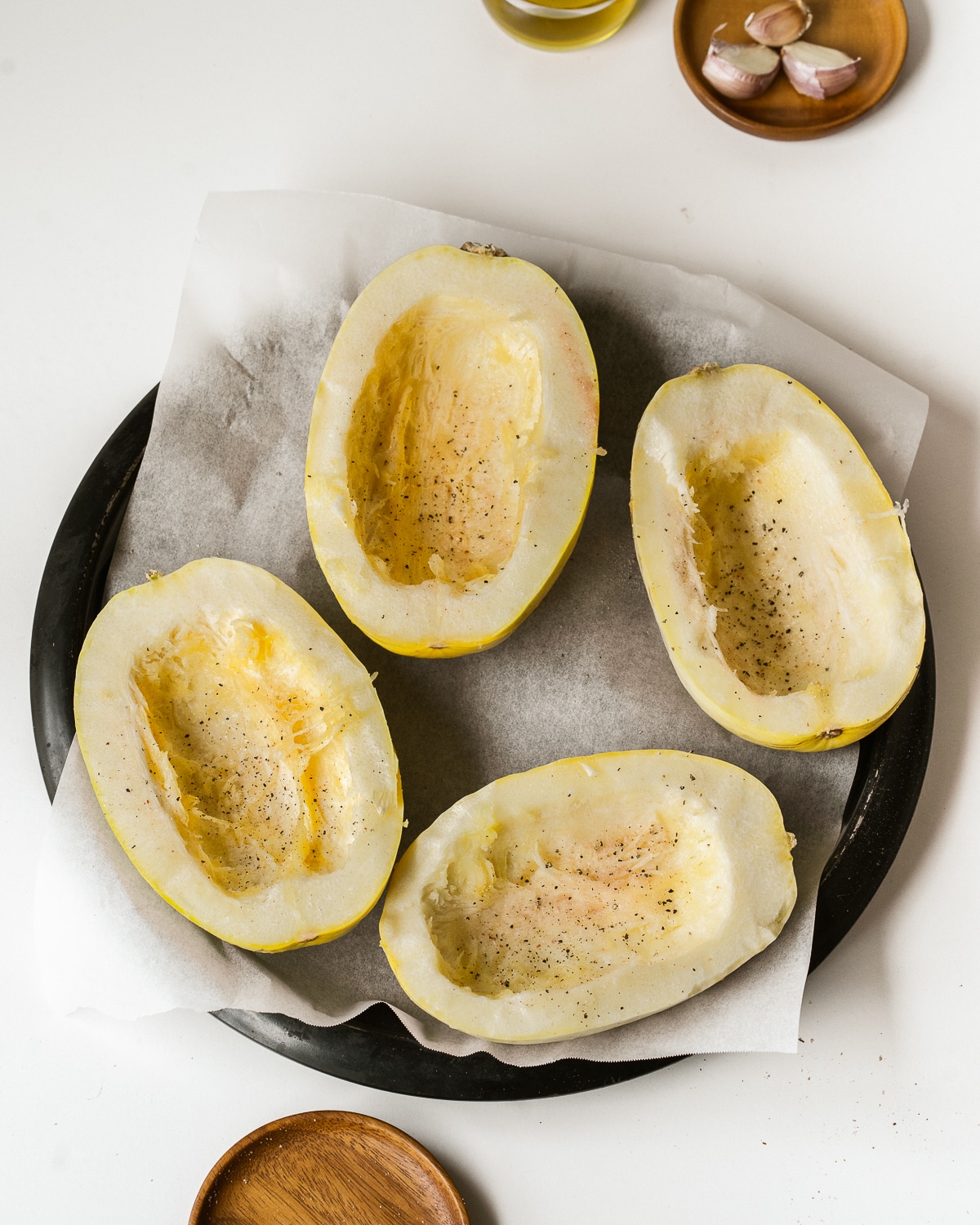 Picture of four spaghetti squash halves on parchment paper on a black tray.