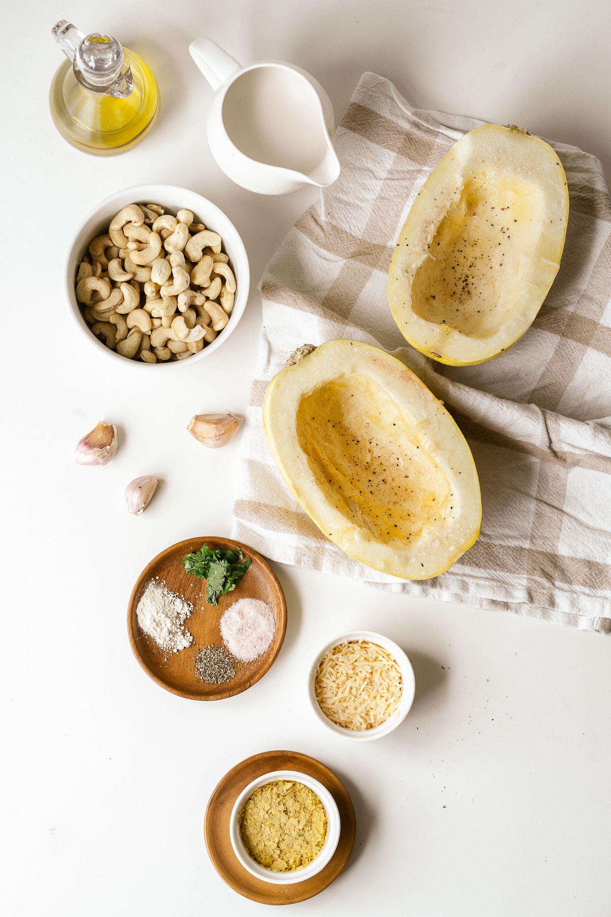 Overhead picture of separate ingredients for Alfredo spaghetti squash some in small white bowls and some on small wooden plates on a white background.