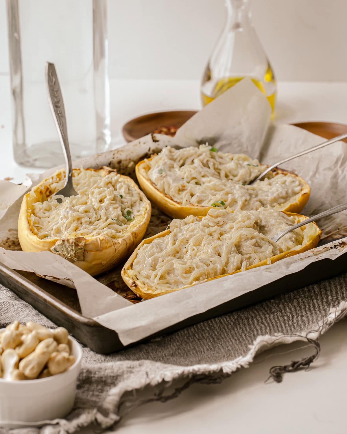 Picture of three halves of Alfredo spaghetti squash with forks in them on a parchment lined baking tray.