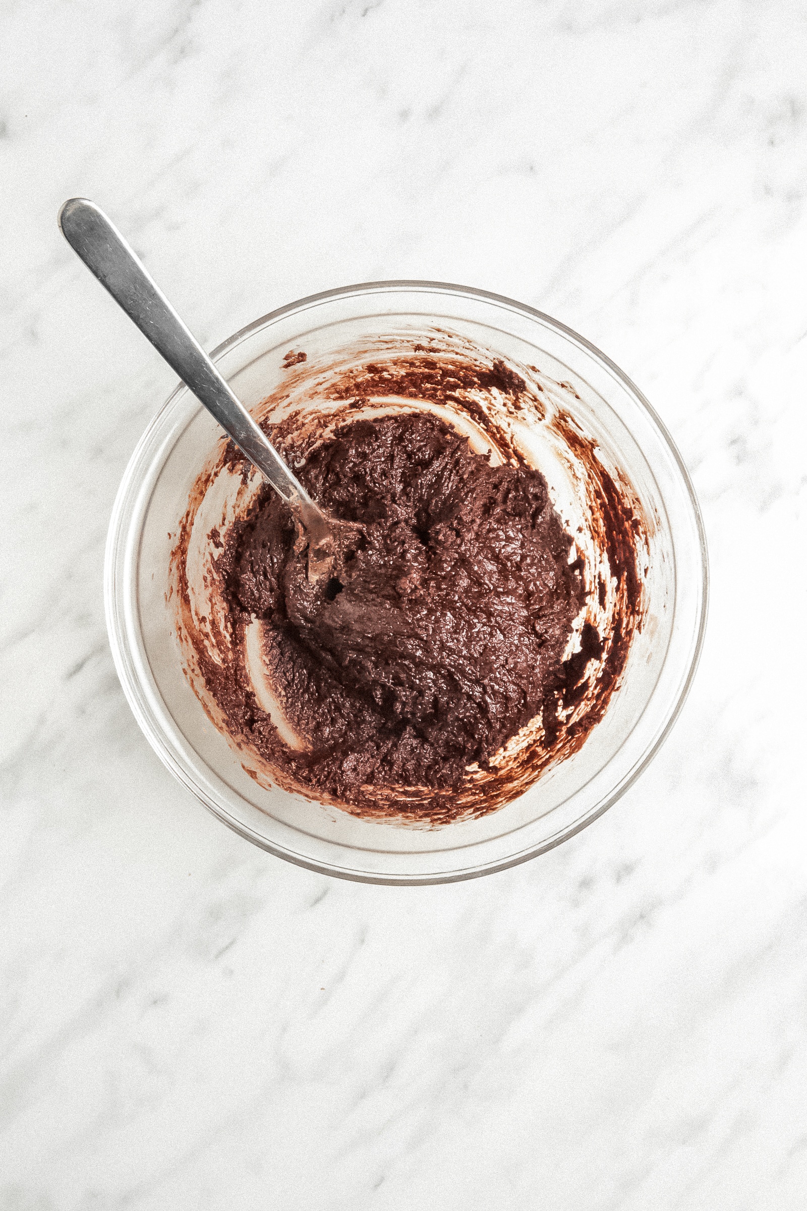 Overhead picture of brownie cookie batter in a glass bowl with a spoon in it.