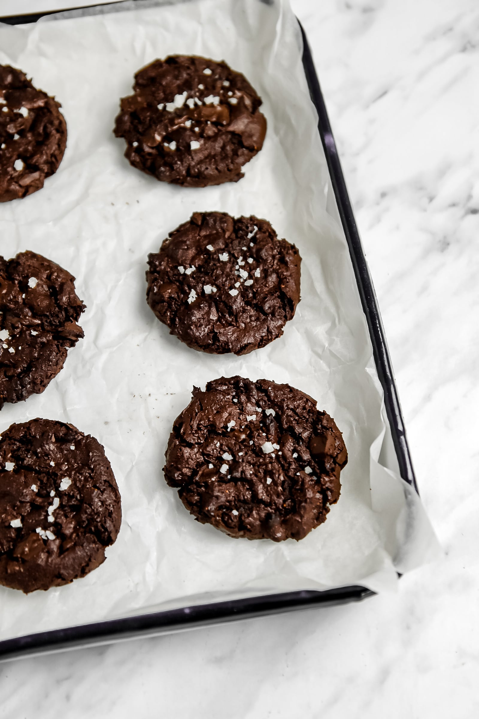 Picture of brownie cookies with sea salt on top and they are on a baking sheet lined with parchment paper.