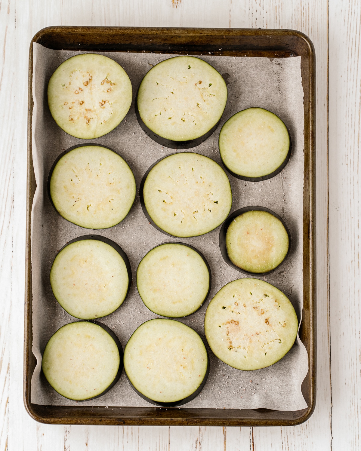 Overhead picture of slices eggplant rounds on a baking sheet lined with parchment paper.