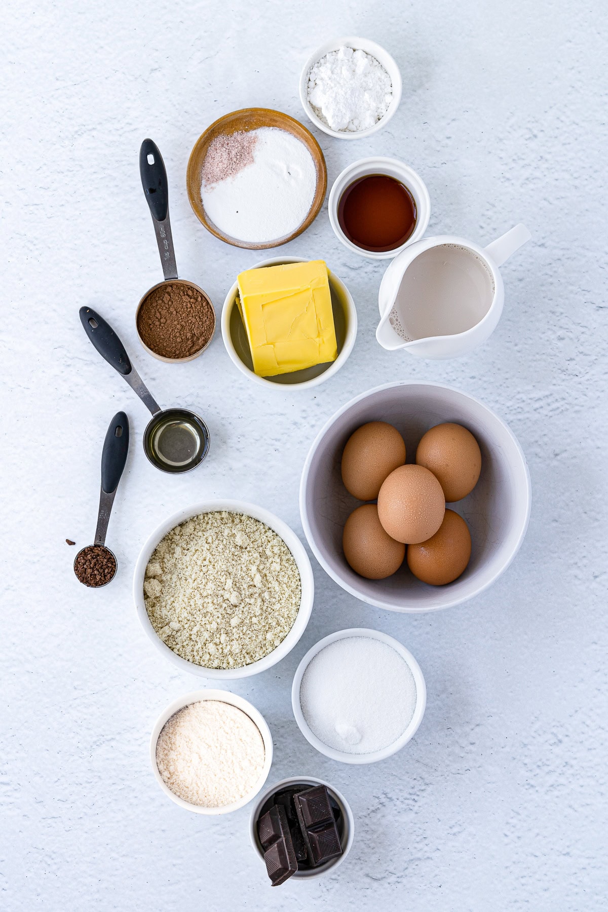 Overhead picture of ingredients for the chocolate mousse cake in individual white bowls and some teaspoons.