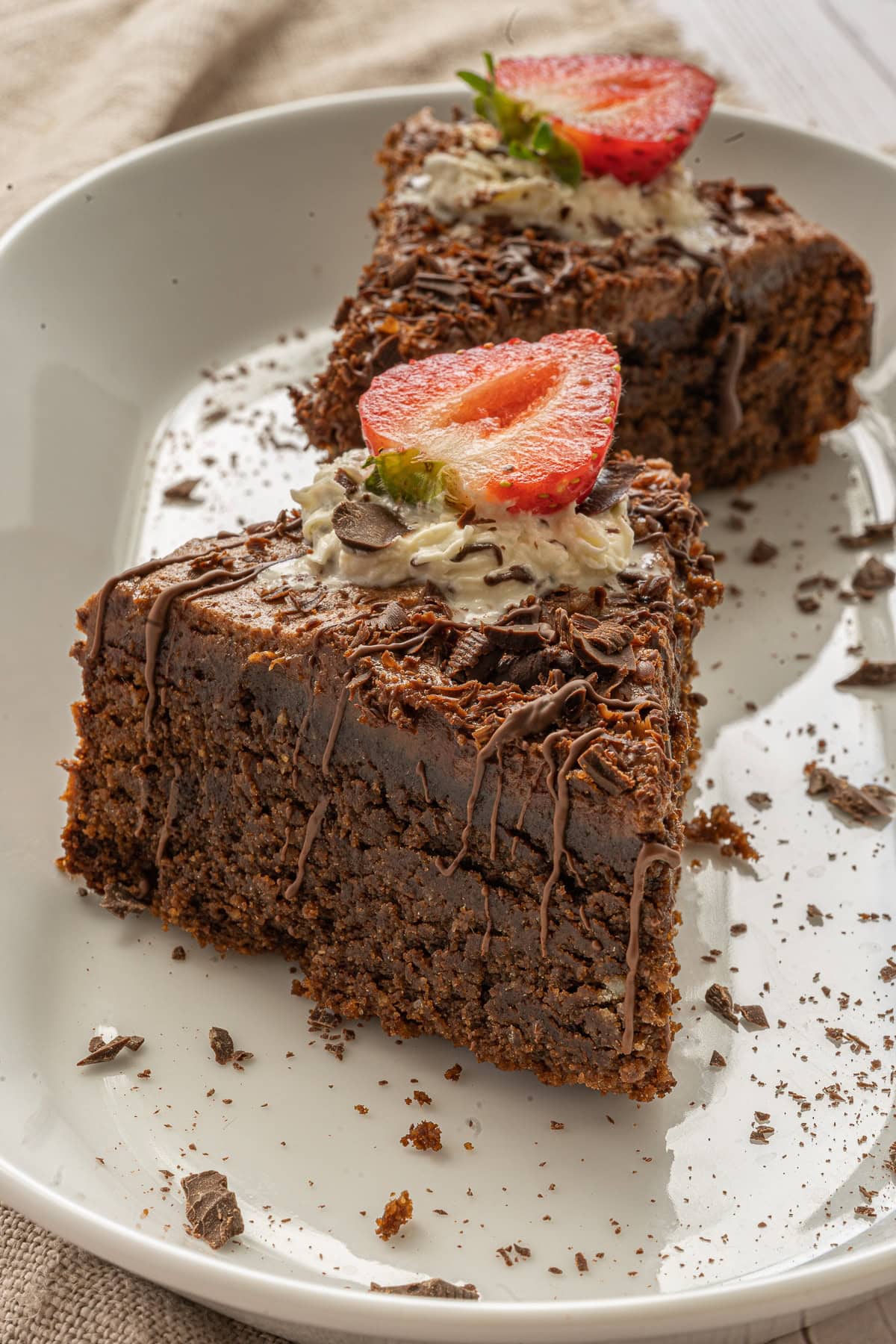 Close up picture of two slices of chocolate mousse cake with a stop of whipped cream and half a strawberry on top and shaved chocolate scattered on the plate.