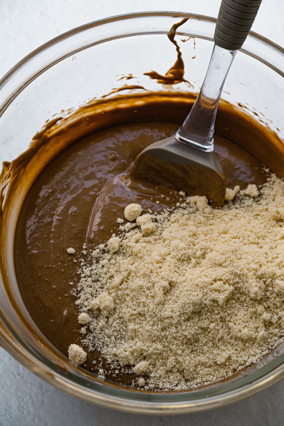 Picture of glass bowl with melted chocolate and wet ingredients and flours sitting on top.