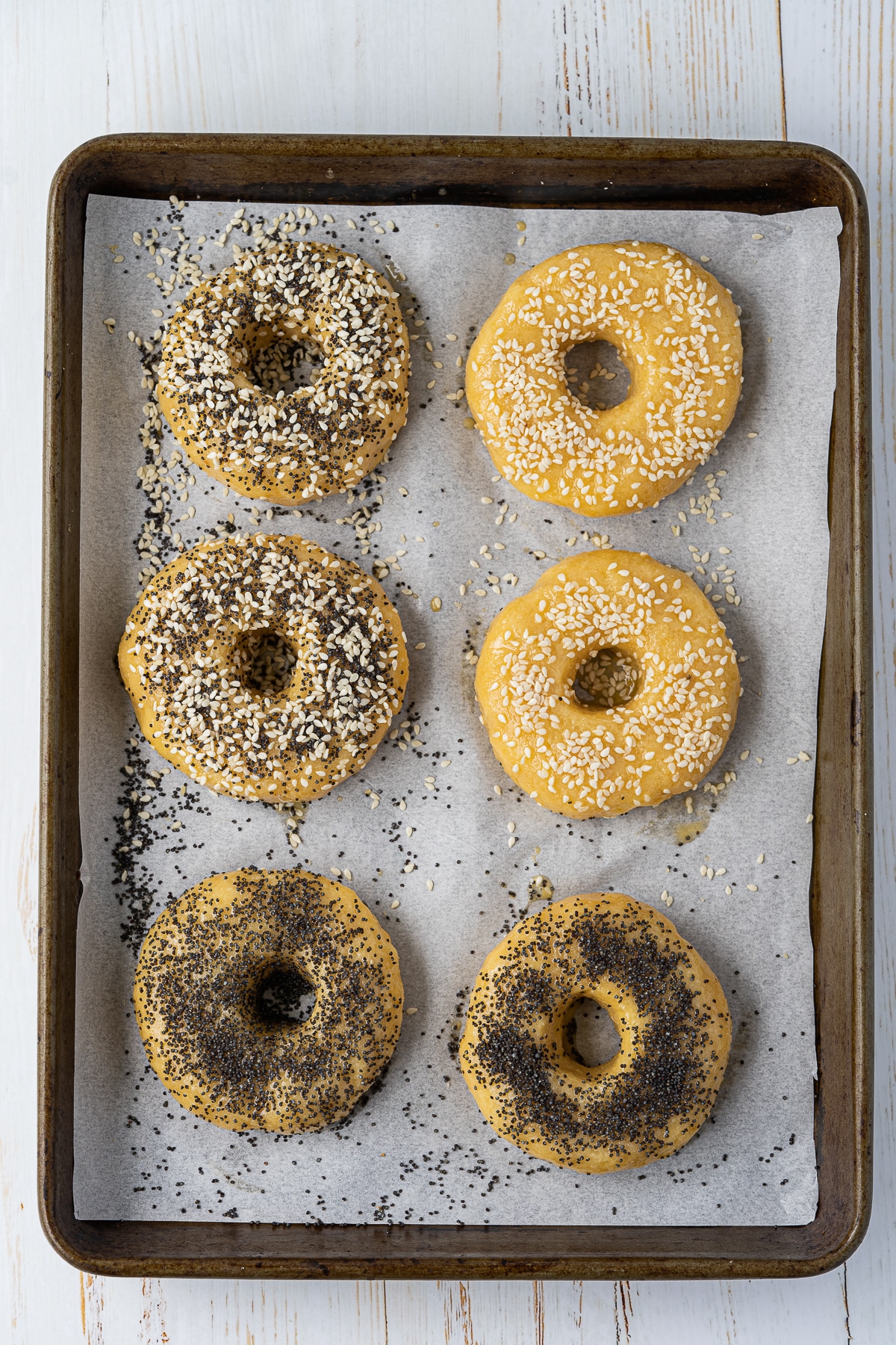Overhead picture of 8 low carb bagels with various seeds and seasonings on them all on a baking tray lined with parchment paper.