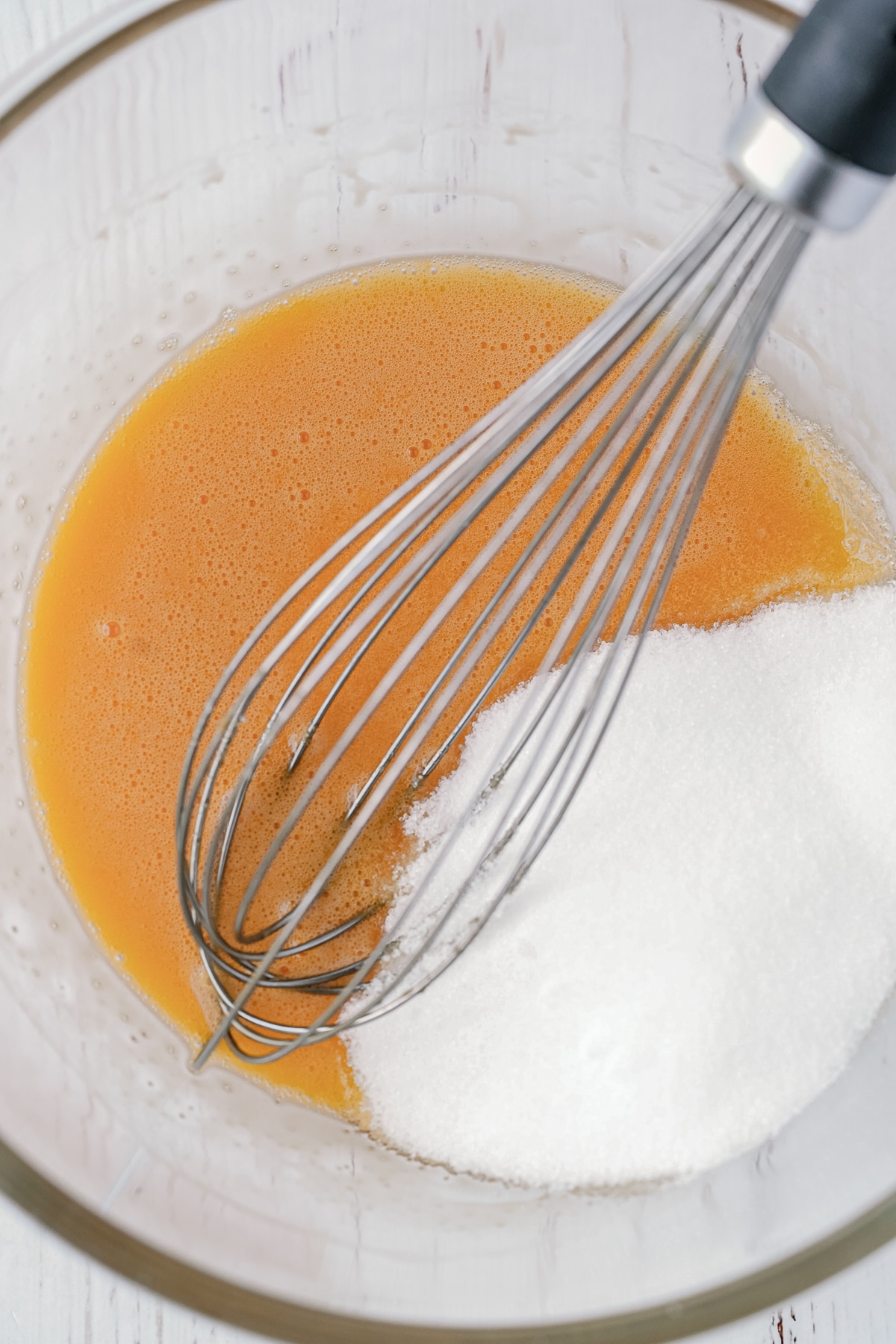 Picture of wet ingredients in a glass bowl and a whisk in there with dry ingredients on top.